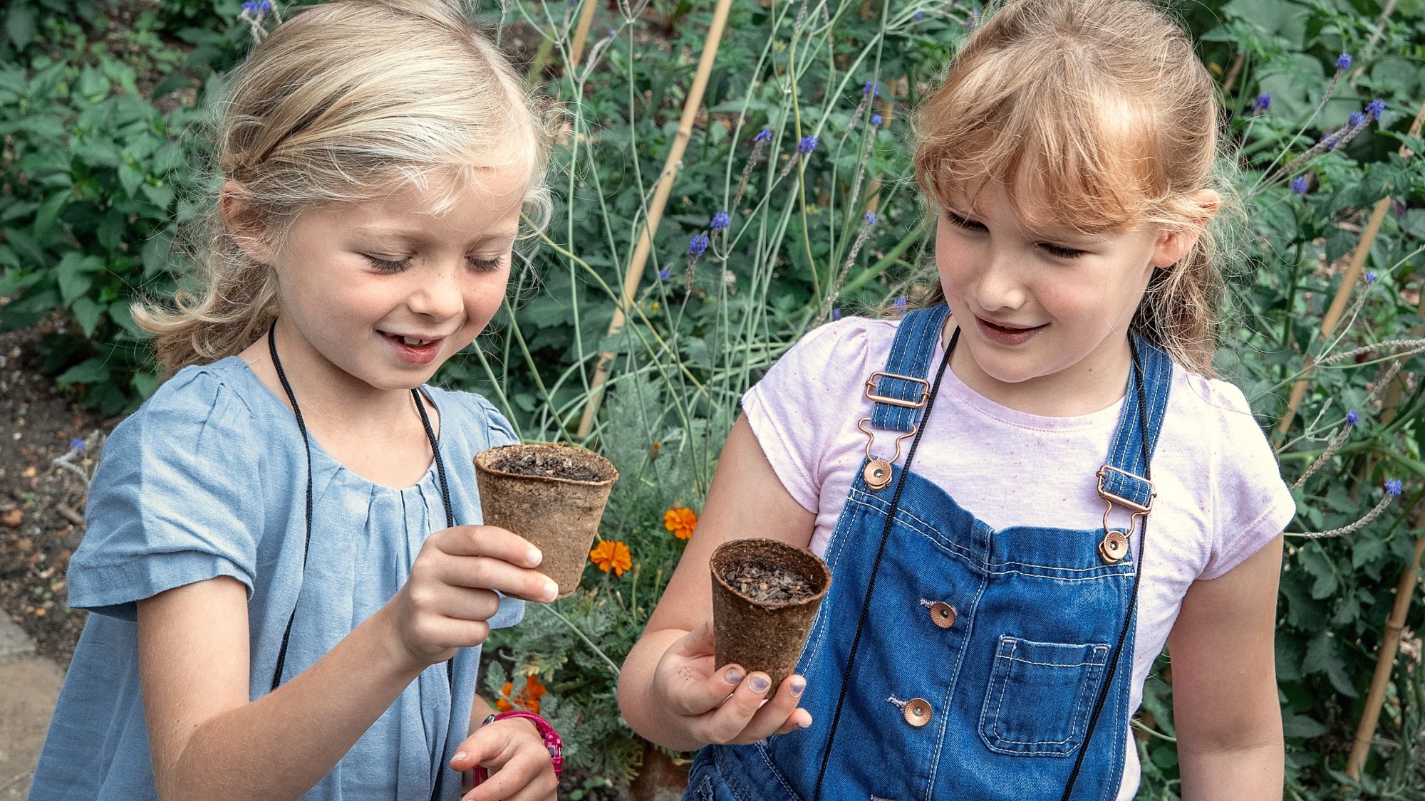 Two young girls hold small plant pots. 