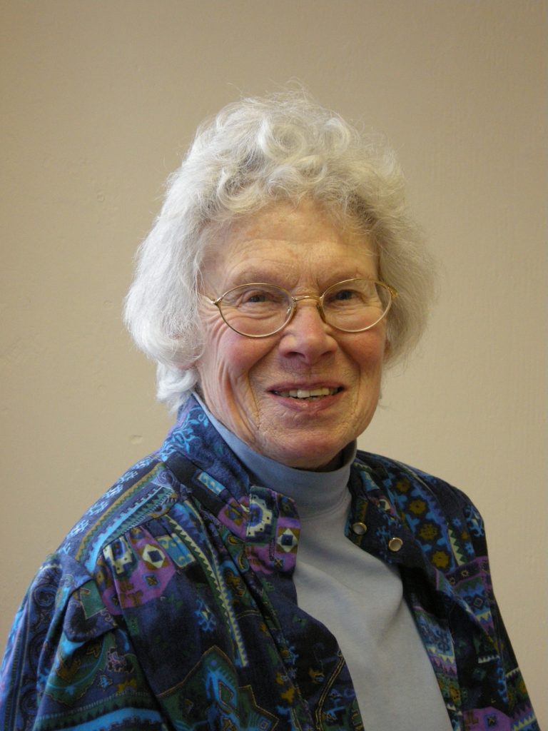 Portrait image of a woman wearing metal rimmed glasses and a blue patterned jacket