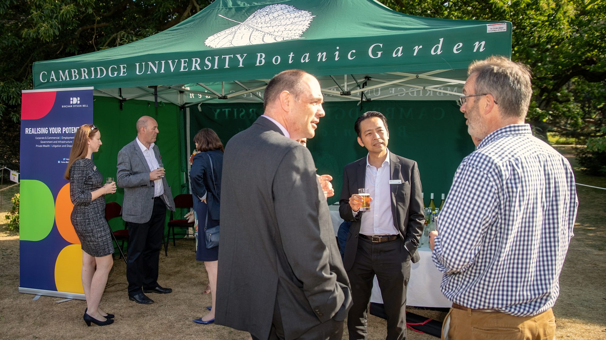 A group of visitors in business attire hold drinks in a Garden.