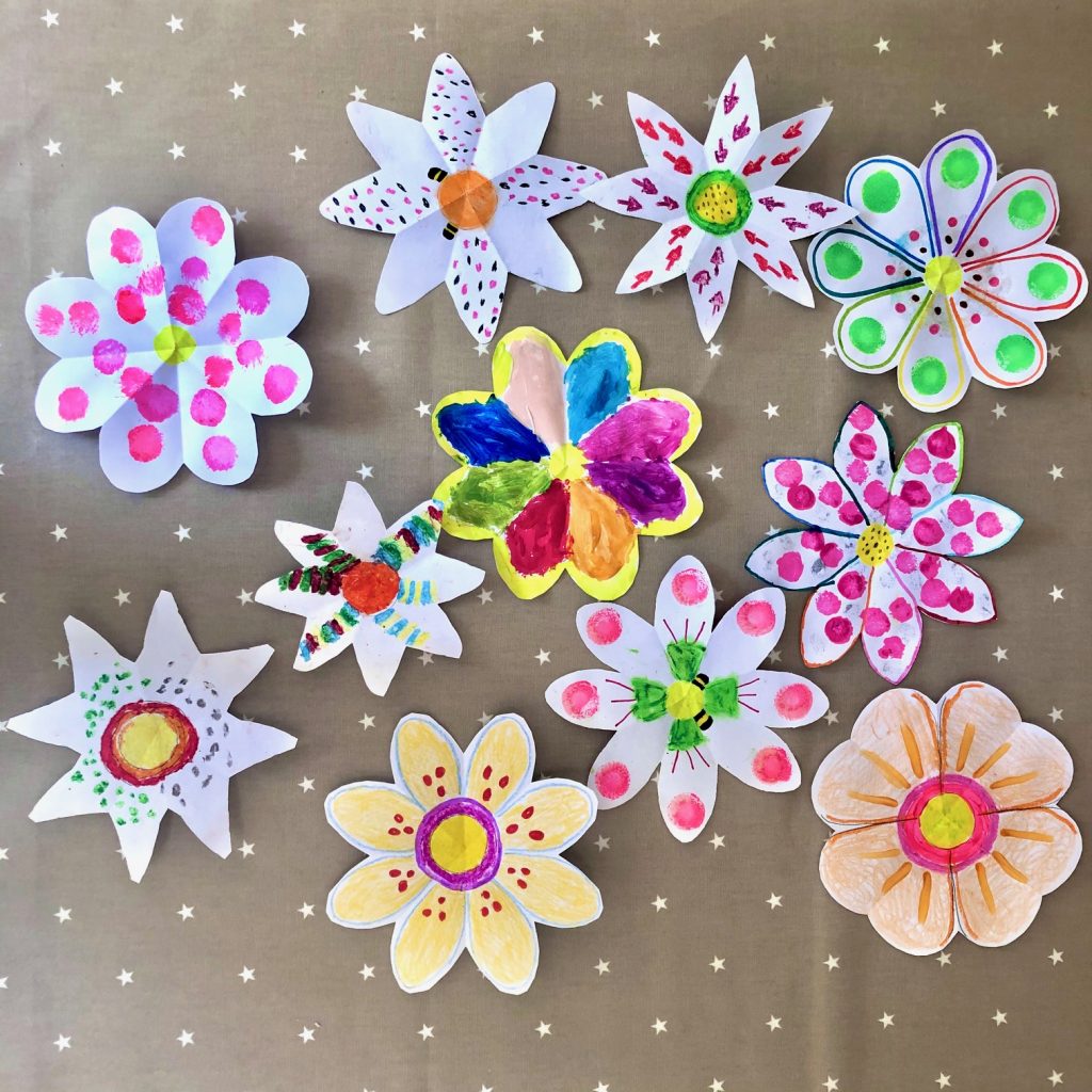 Different symmetrical flowers cut out from paper and decorated with coloured pens and pencils.