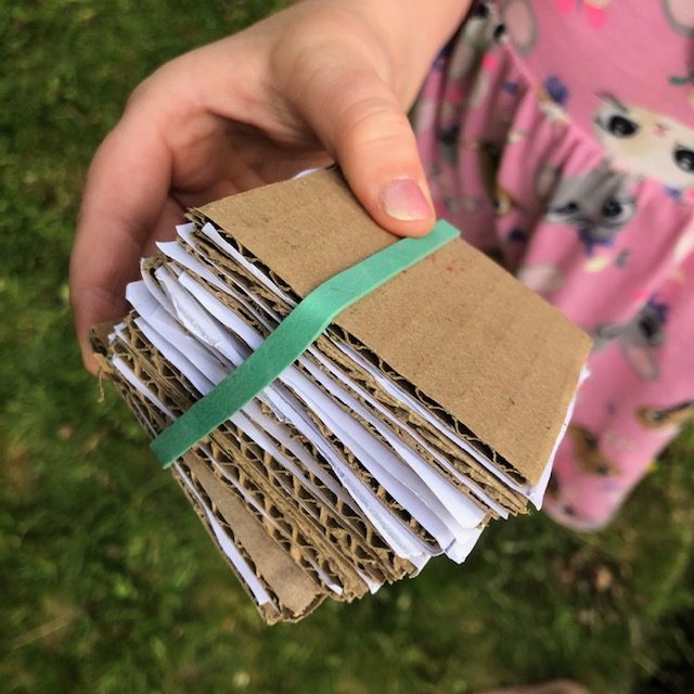 A homemade flower press made of bits of cardboard and paper held together by an elastic band.