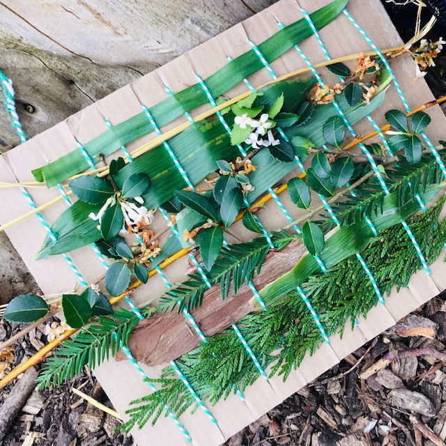 A handmade loom with different leaves and branches woven between string.