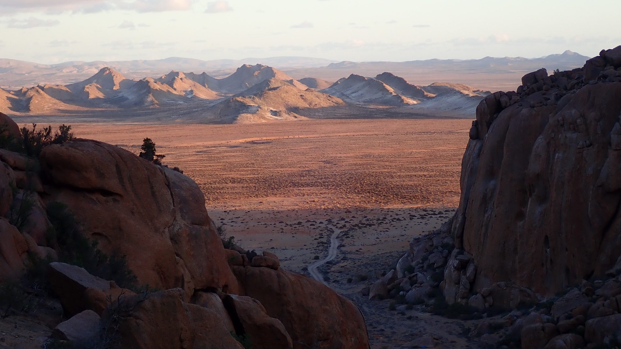 Mountains are dotted among a red plateau that stretches far into the distance.