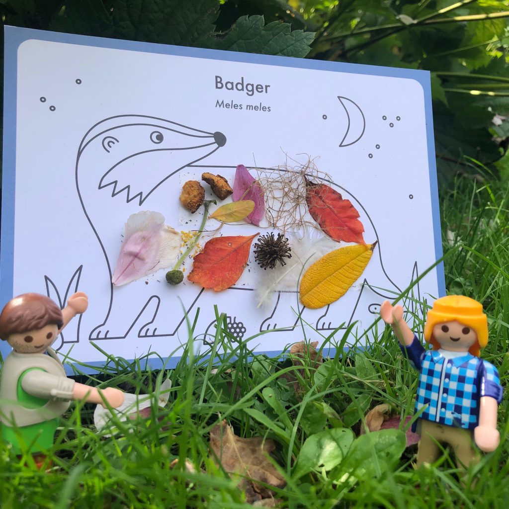 Two small figurines point at an illustration of a badger decorated with leaves and flowers.