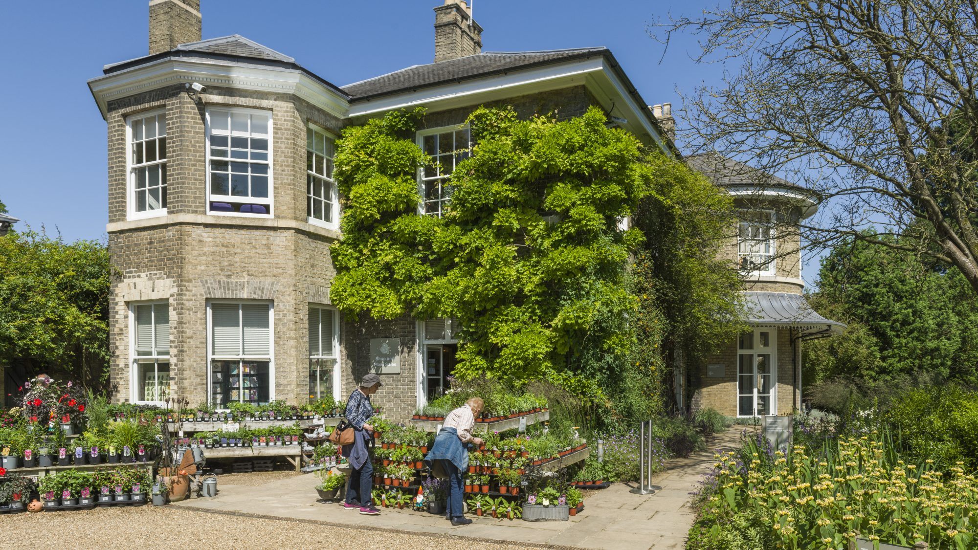 The Garden's Brookside building and shop entrance with some visitors looking at the plants for sale outside