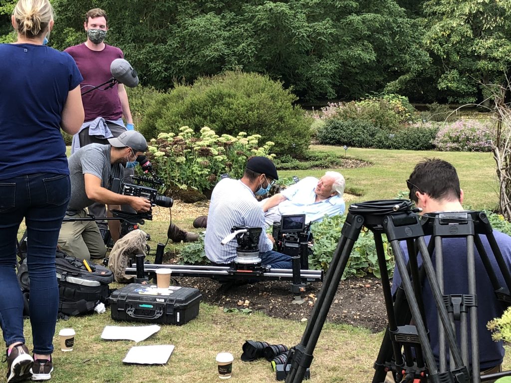 Sir David Attenborough lying next to the squirting cucumbers with the film crew around him