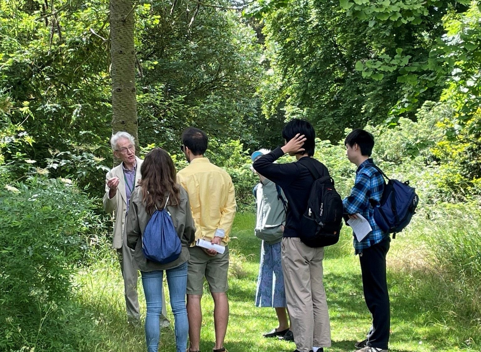 A group of visitors in a wooded area listening to a tour guide.