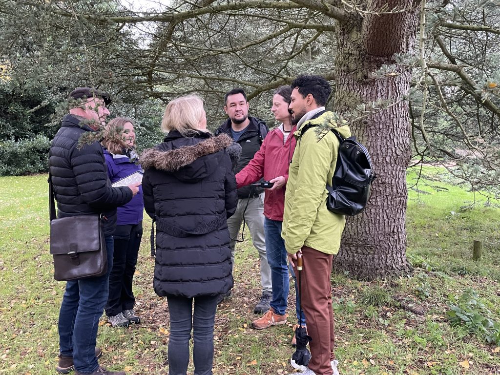 GQT team stand in a circle around the radio microphone underneath a tree in the Garden.
