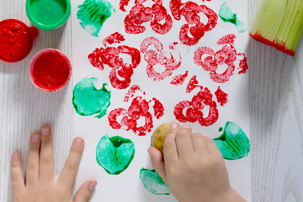 A child printing in red and green ink using a potato and celery