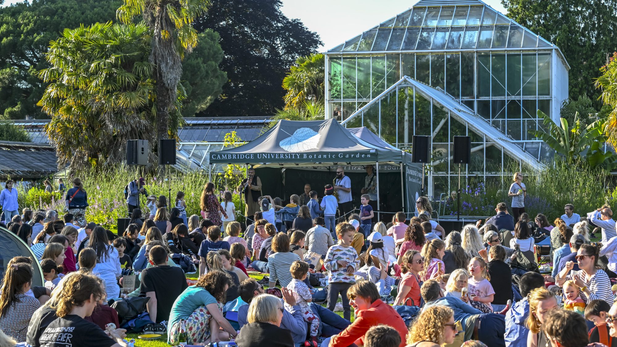 A view of musicians in a marquee playing to a Garden of visitors on a summer evening. 